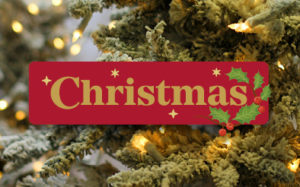 The word 'Christmas' is seen written on a red banner against a background photo of a Christmas Tree.