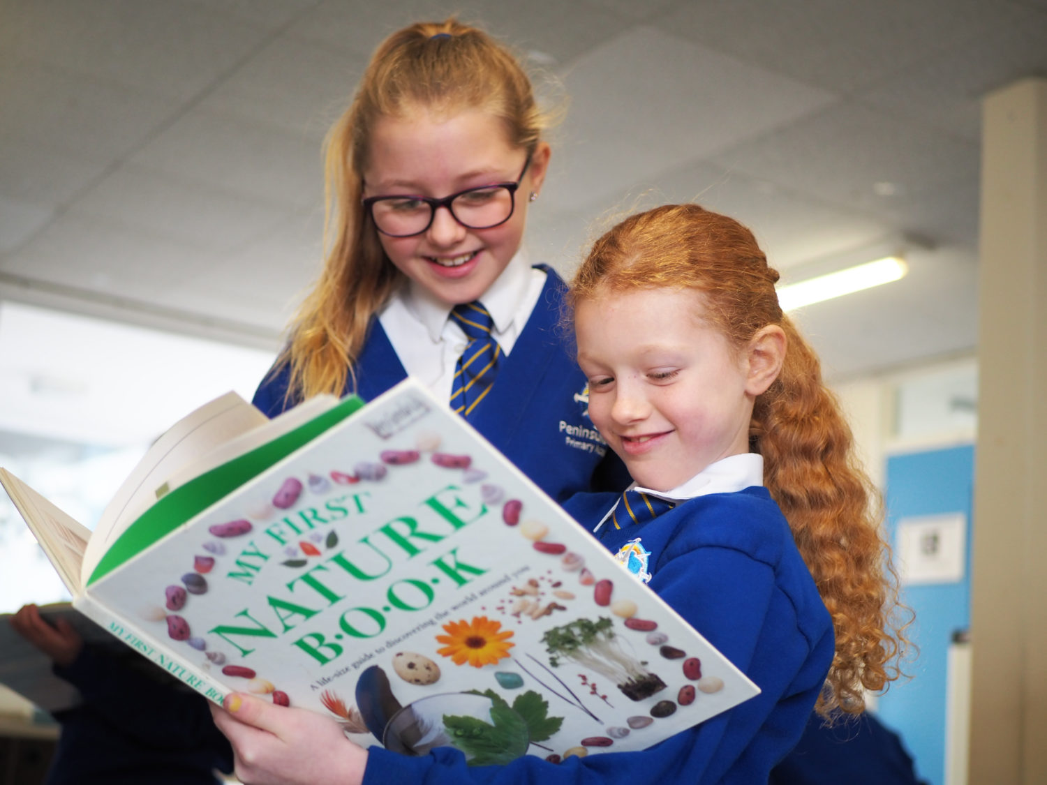 Two young girls are pictured smiling together whilst reading a large picture storybook.