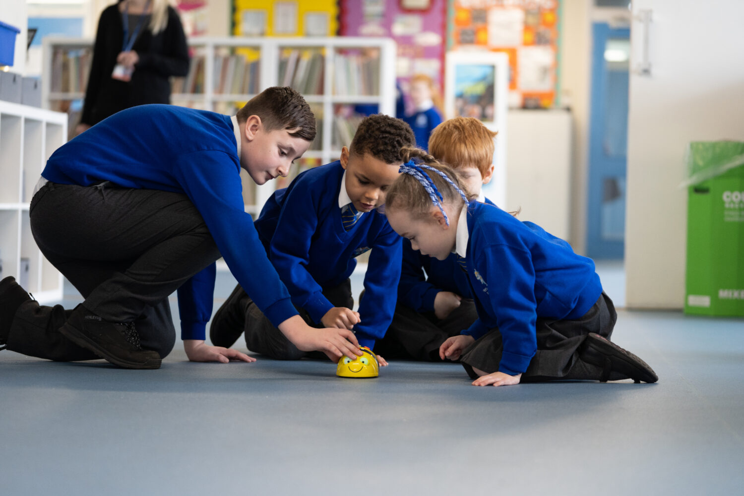 A group of four pupils, male and female, are pictured playing together on the floor with a Bee-shaped toy.