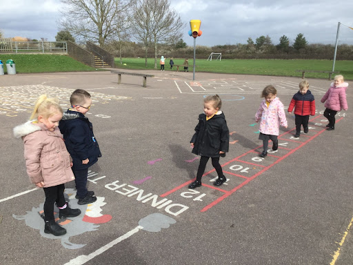 A group of young Nursery children are seen playing outdoors, wearing their winter coats.