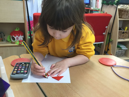 A Nursery child sat at a table writing with a pencil.