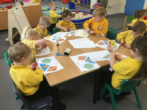 A group of nursery children sat around a table cutting and gluing paper.