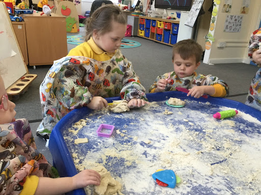 Nursery children around a table playing in sand.